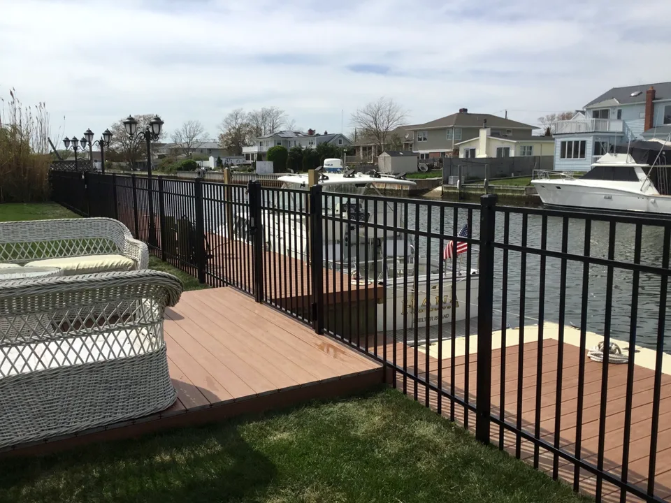 Black aluminum fence following the waterfront bulkhead beside a deck in Mastic Beach, New York.