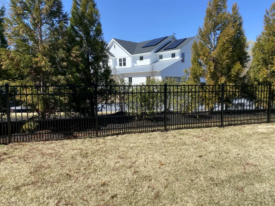 Four-foot black aluminum estate fence with puppy pickets shown with a Remsenburg, New York residence beyond.