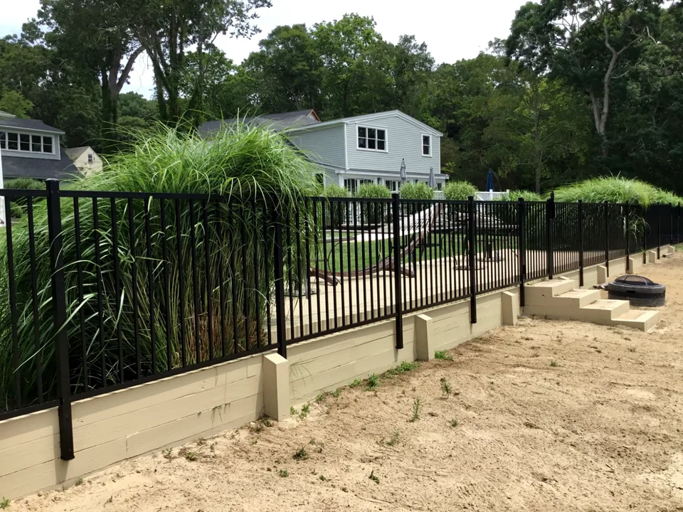 Four-foot black aluminum backyard fence shown beside a retaining-wall area in Mattituck, New York.