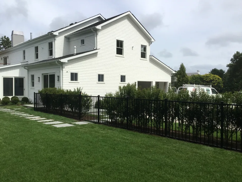 Black aluminum perimeter fence running through landscaped grounds in Southampton, New York.