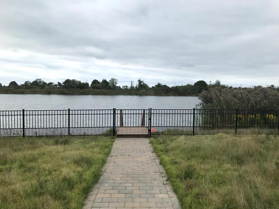 Black aluminum gate within a four-foot puppy-picket fence in Sag Harbor, New York, with water visible beyond the property.