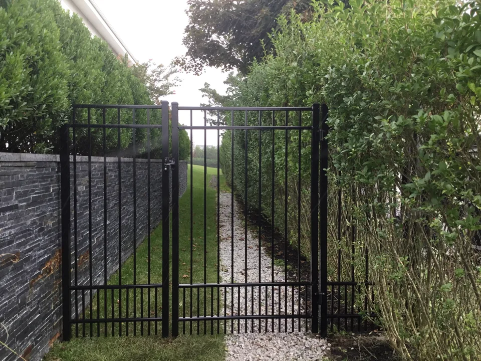 Black aluminum walk gate within a tall residential fence installation in Westhampton, New York.