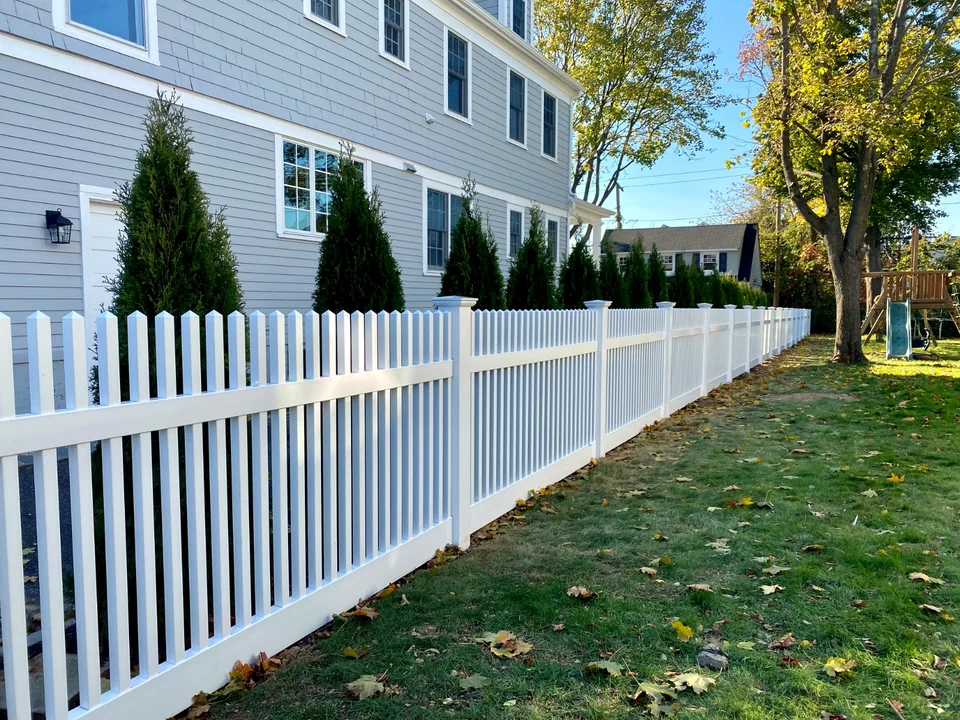 Long side-yard run of white PVC picket fencing beside a Brightwaters home.