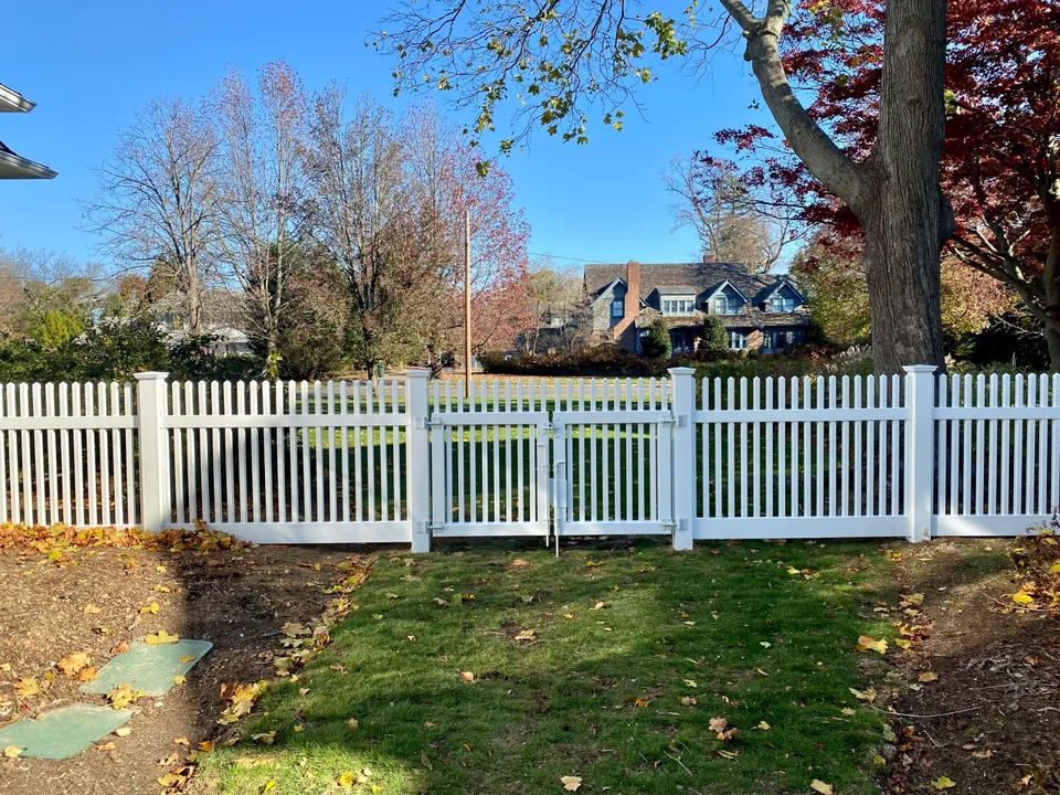 White PVC picket fence with a matching walk gate across a Brightwaters, New York yard.