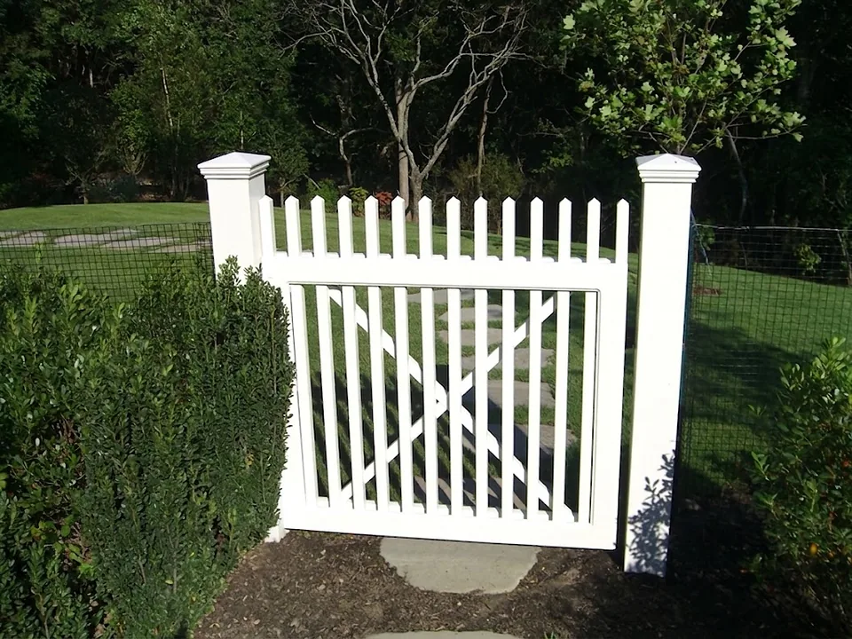 White cedar Victorian gate with a scalloped picket top and an internal X brace, hung between capped posts on a stepping stone path in Montauk, New York