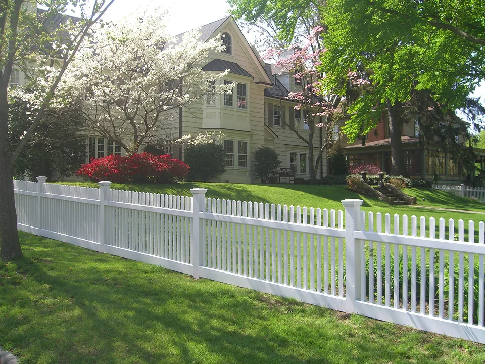 Four-foot cedar Victorian picket fence stained white running along a front lawn beneath flowering dogwoods in Larchmont, New York
