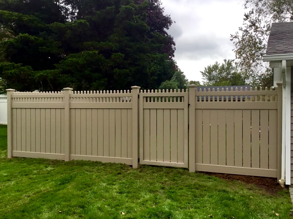 Tan PVC privacy fence with decorative picket top and matching walk gate in Coram, New York.