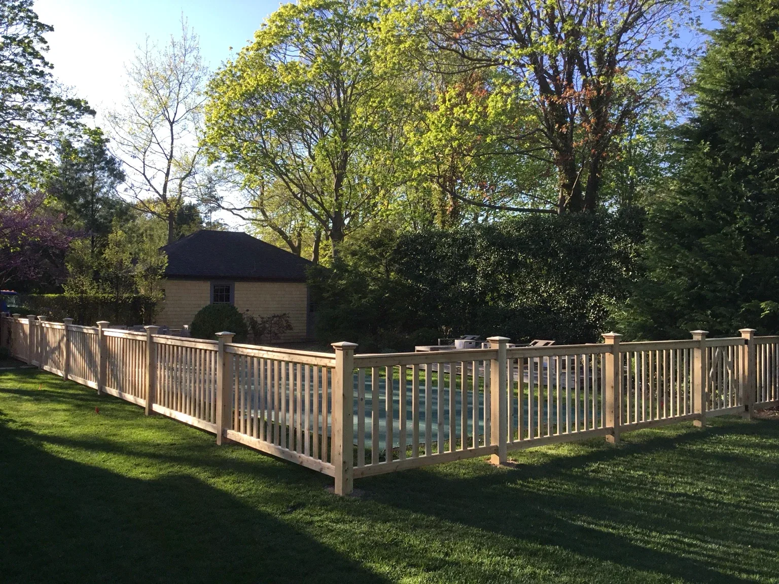 Custom white cedar fence surrounding a landscaped backyard in Bellport Village, New York