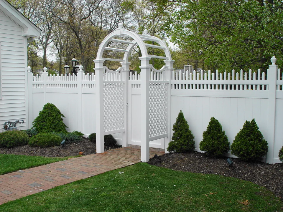 Decorative white PVC arbor integrated into a six-foot privacy fence with alternating spindle top in Holbrook, New York