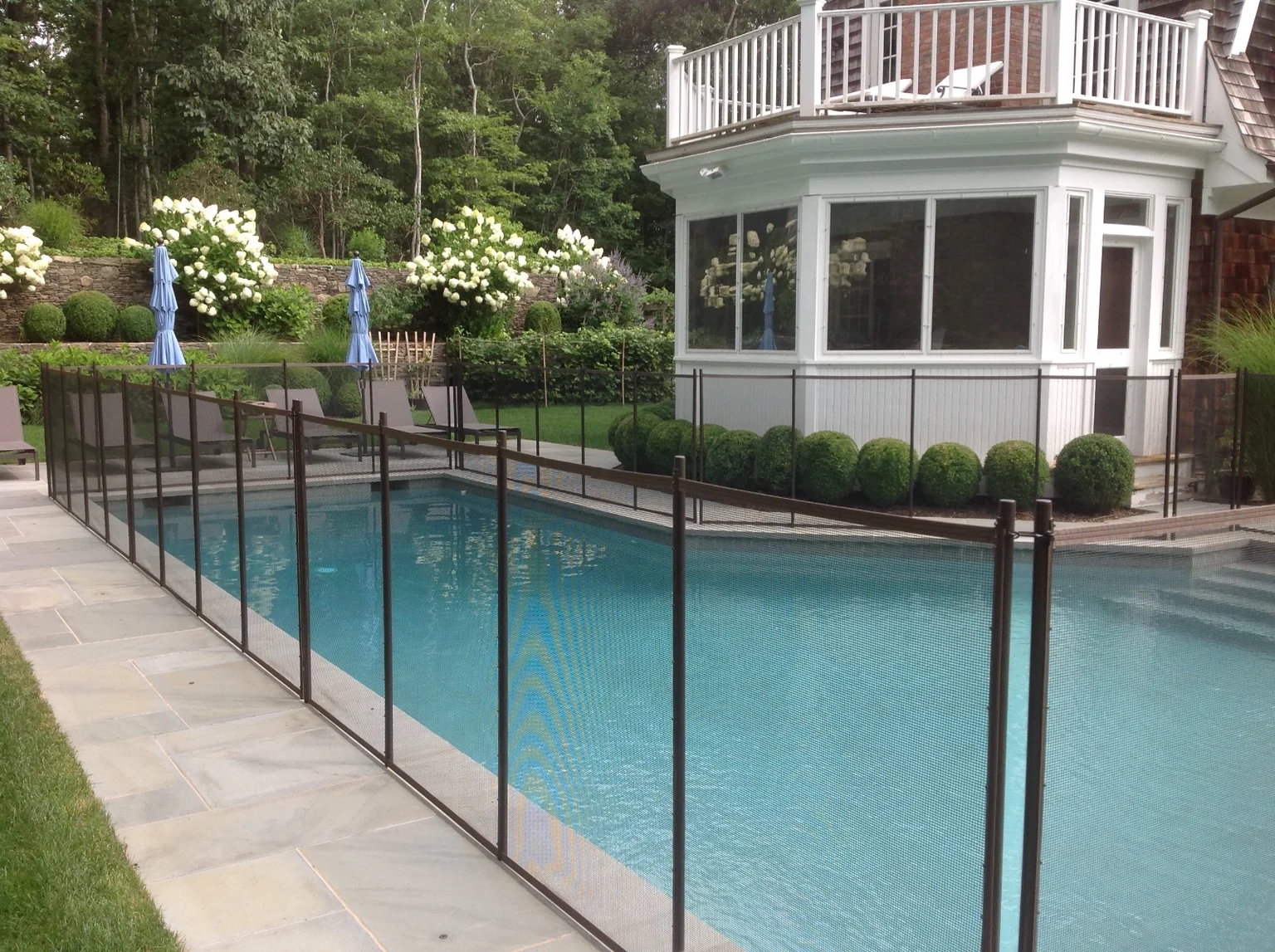 Brown Guardian removable mesh pool fence running along the East Hampton pool with the home and landscaped stone wall beyond