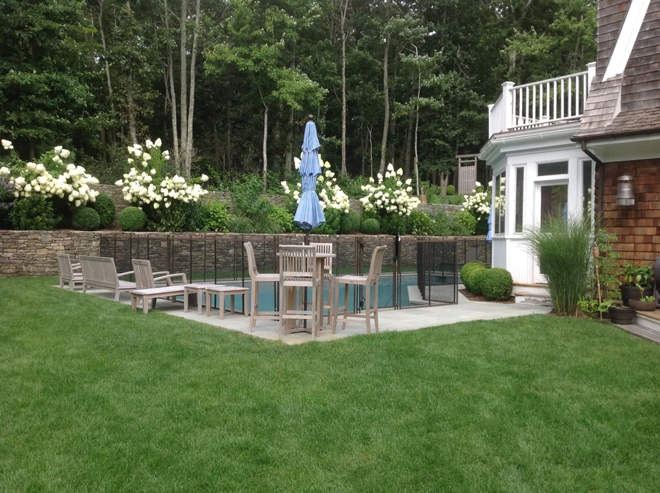 Wide lawn view of the brown Guardian pool fence beside the East Hampton home and landscaped pool area
