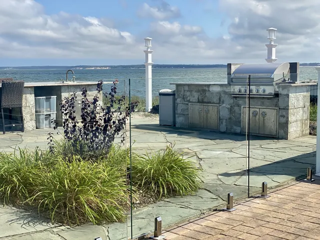 Frameless glass pool fence beside a waterfront outdoor kitchen in Southold, New York.