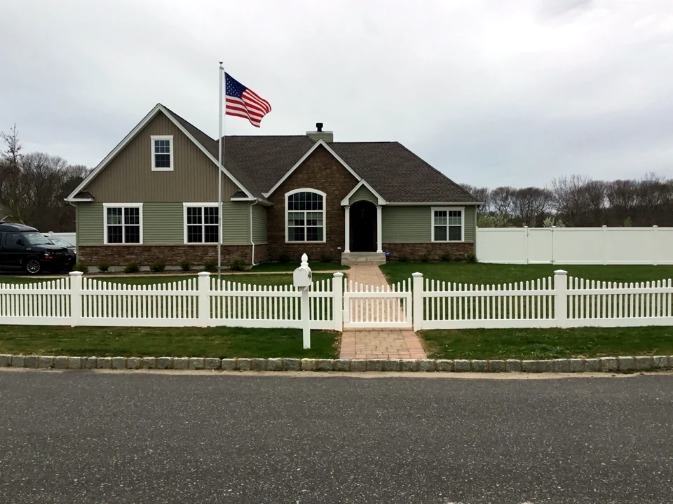 Three-foot white scalloped PVC picket fence across the front of a Manorville, New York home.