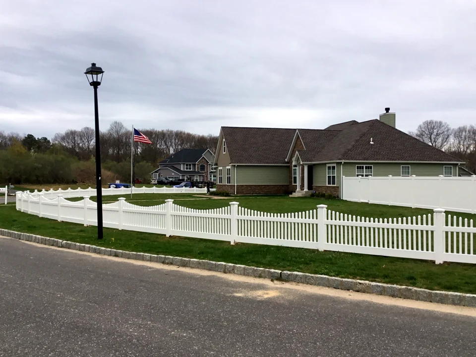 Three-foot white PVC picket fence turning a corner around a Manorville property.
