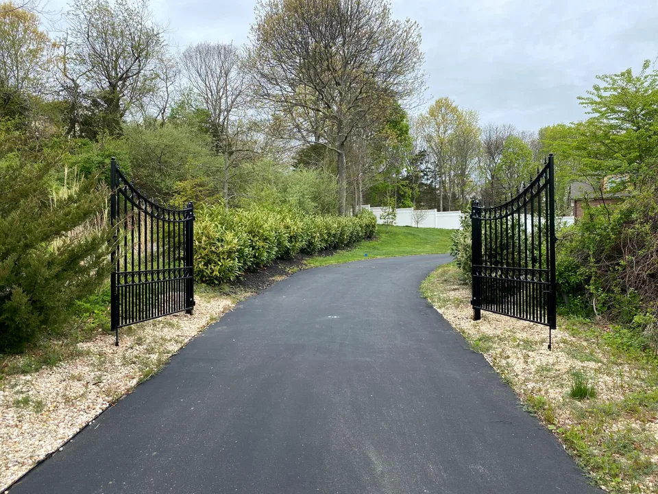 Open black ornamental steel double-drive estate gate at a landscaped driveway entrance in Calverton, New York.
