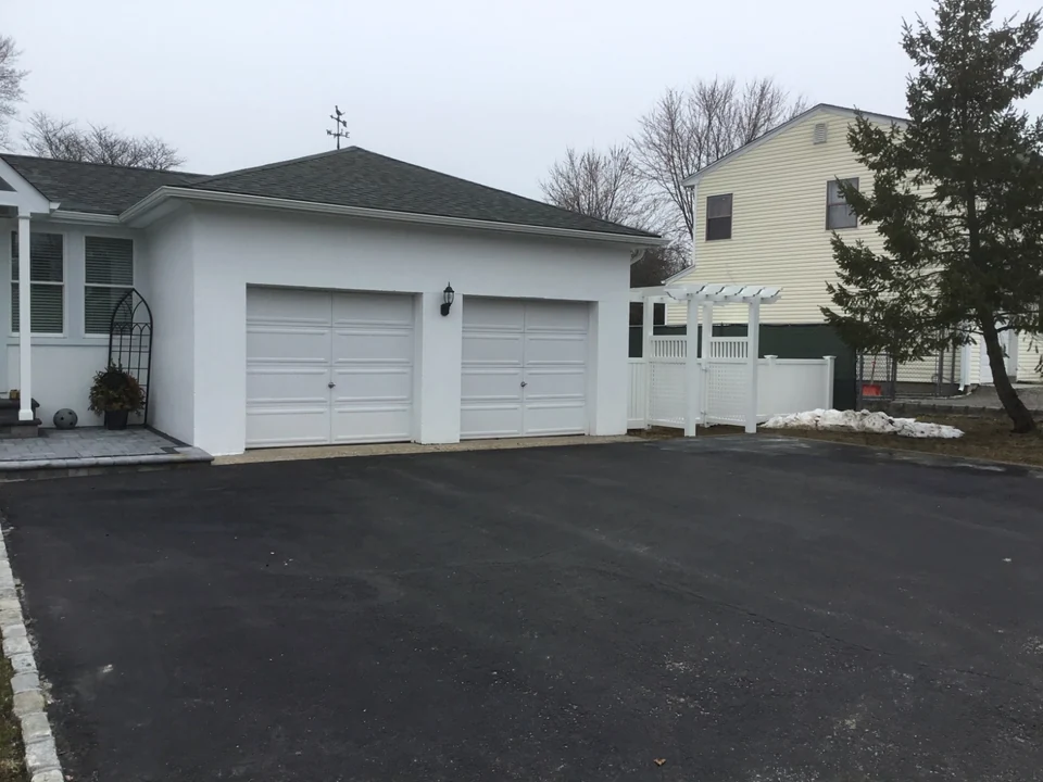 Wide driveway view of a white PVC arbor gate and semi-privacy fence beside a detached garage in Patchogue, New York