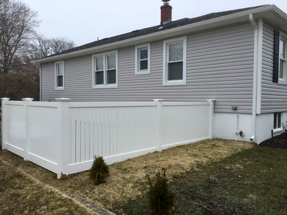 Four-foot white New Jersey semi-privacy PVC fence field-fitted along a changing grade beside a Patchogue home