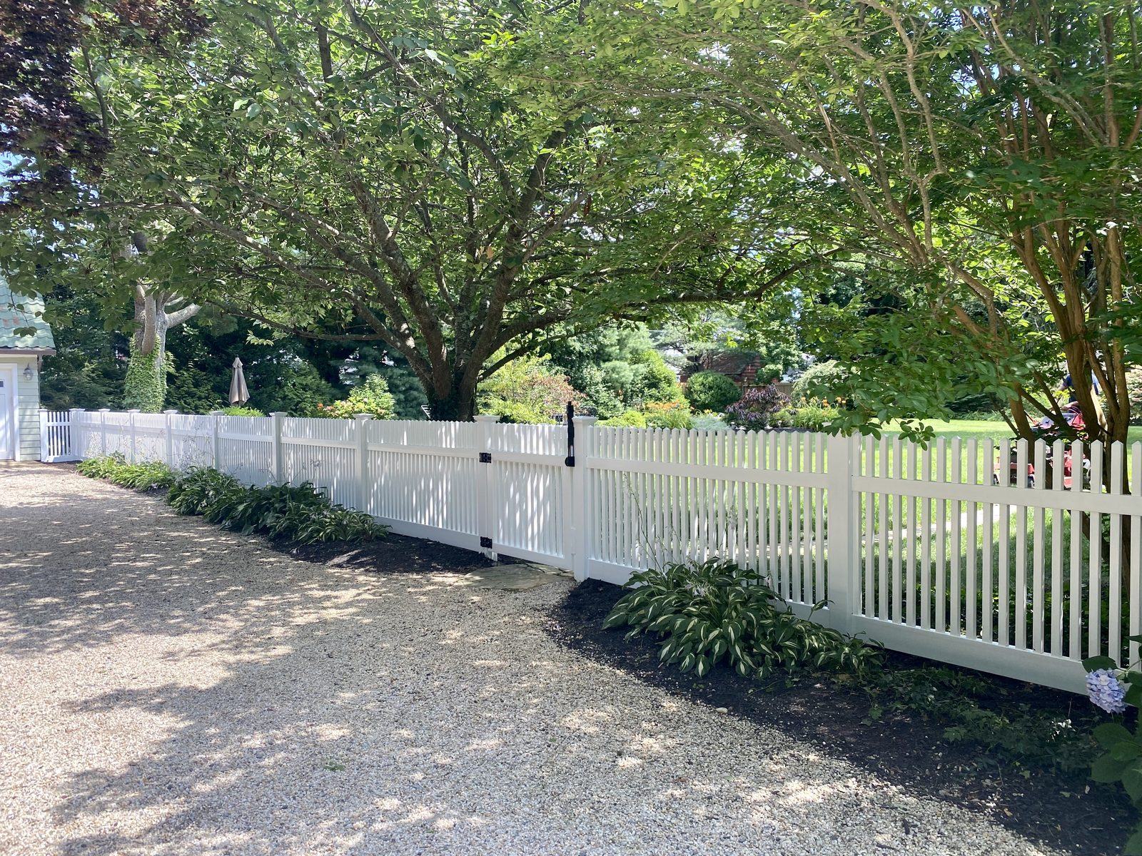 Custom white PVC picket fence installation with matching gate along a residential property in Suffolk County, NY