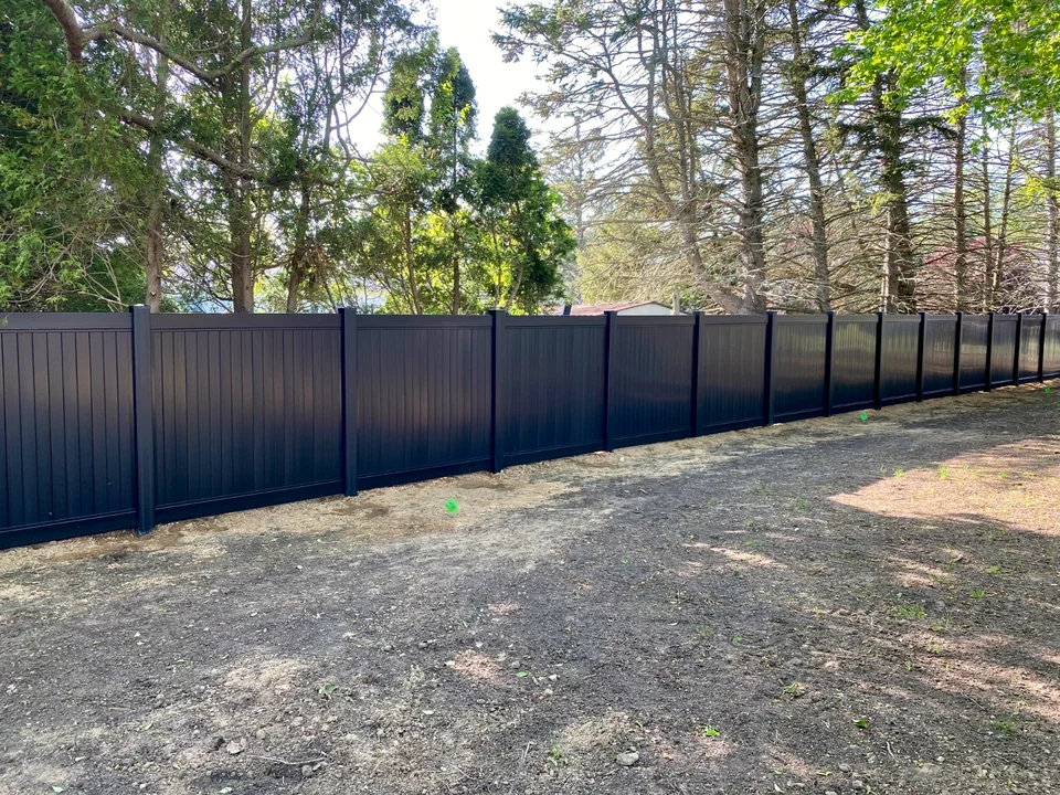 Long straight run of six-foot black PVC privacy fence across a Southold, New York property.