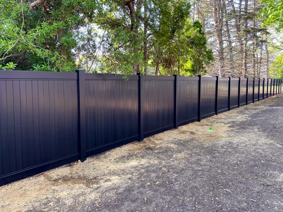 Long run of six-foot Blackline black PVC privacy fence in a wooded Southold, New York yard.