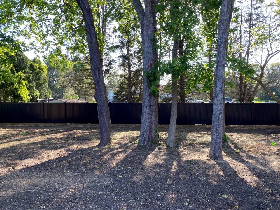 Wide wooded-yard view of a six-foot black PVC privacy fence in Southold, New York.
