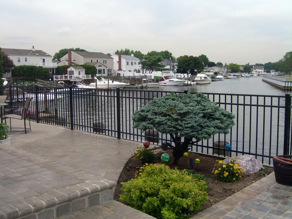 Black aluminum waterfront fence following the canal edge at a raised patio in Seaford, New York