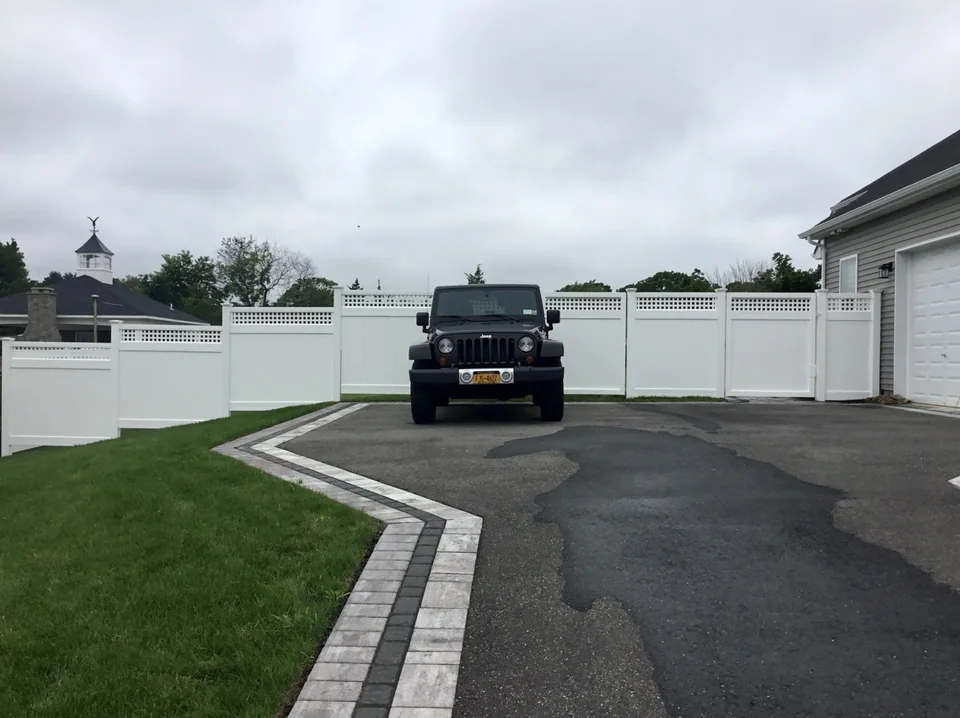 White PVC privacy fence with square lattice top stepping through grade changes beside a driveway in Wading River, New York